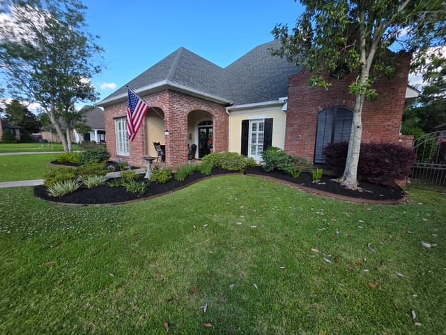 Brick home facade with black mulch landscaping and striped lawn